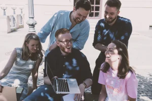 Fünf Personen, die zusammen an einem Laptop arbeiten und dabei lächeln.